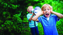 Little boy covering his ears while his brother is yelling on him with megaphone.