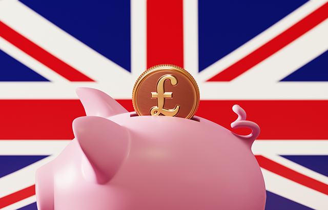 Piggy bank and pound coin over British flag background. Horizontal composition with copy space. Great use for savings concepts.